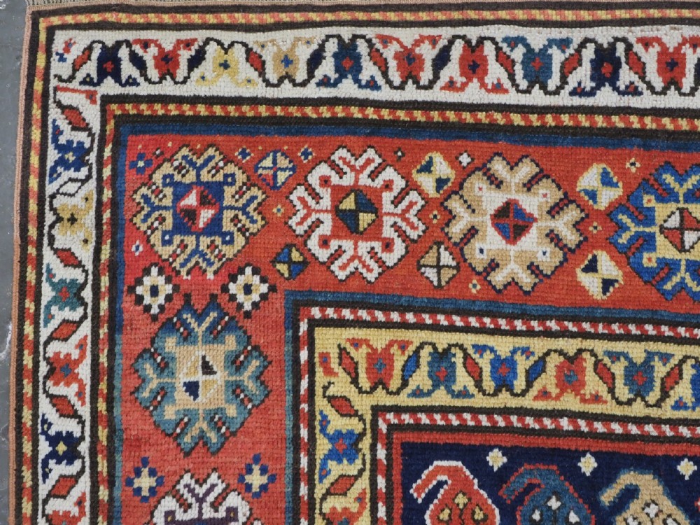 An antique hand-knotted Caucasian runner rug featuring repeated boteh motifs on a dark blue central field framed by red geometric borders. View VI