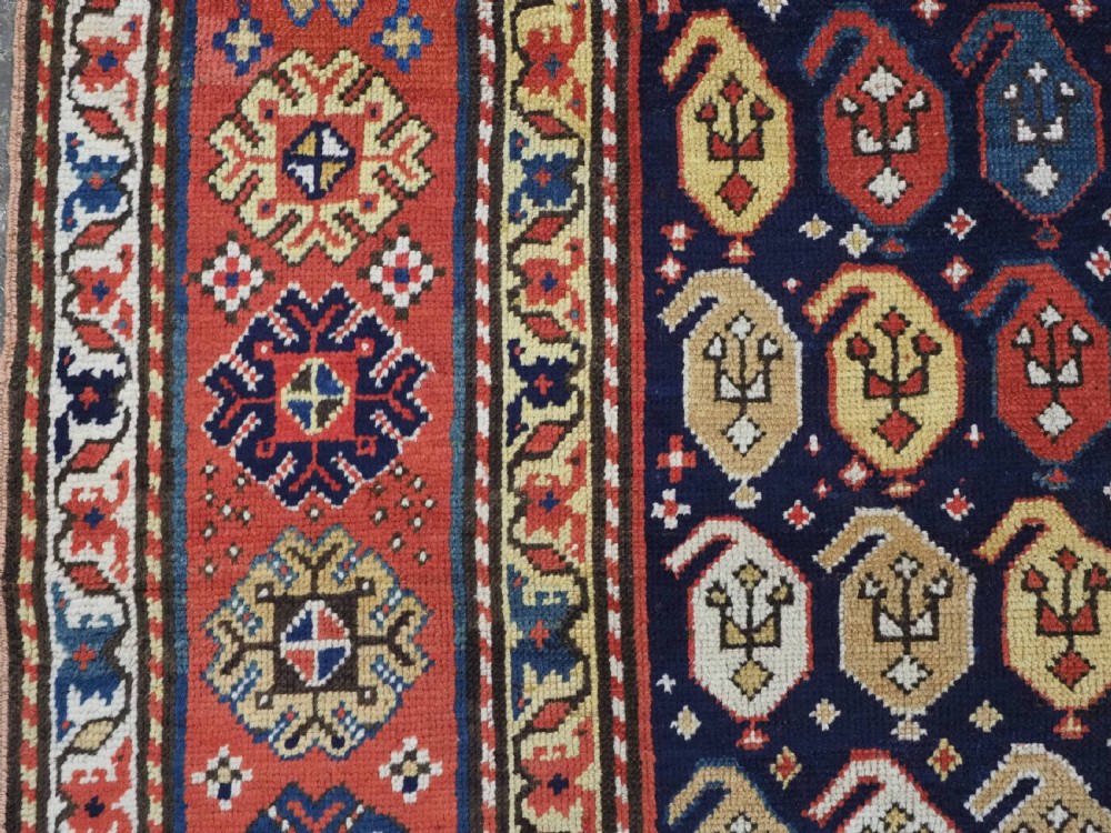 An antique hand-knotted Caucasian runner rug featuring repeated boteh motifs on a dark blue central field framed by red geometric borders. View VII