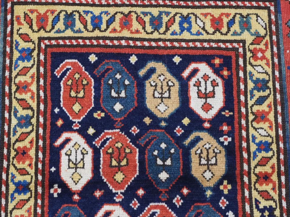 An antique hand-knotted Caucasian runner rug featuring repeated boteh motifs on a dark blue central field framed by red geometric borders. View VIII