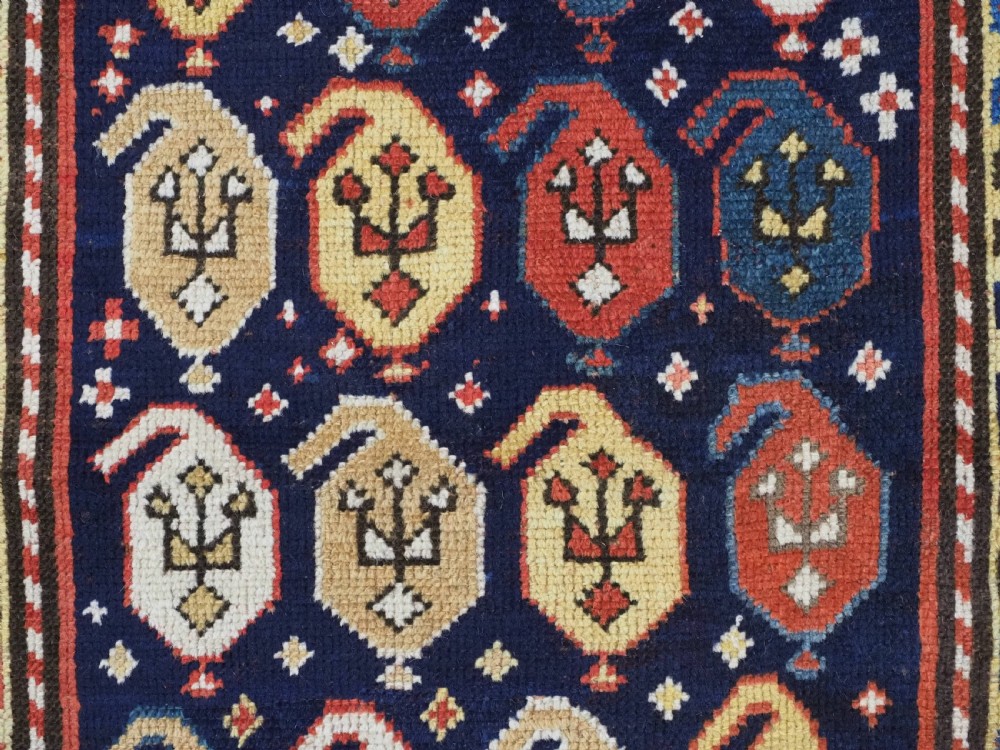 An antique hand-knotted Caucasian runner rug featuring repeated boteh motifs on a dark blue central field framed by red geometric borders. View IX