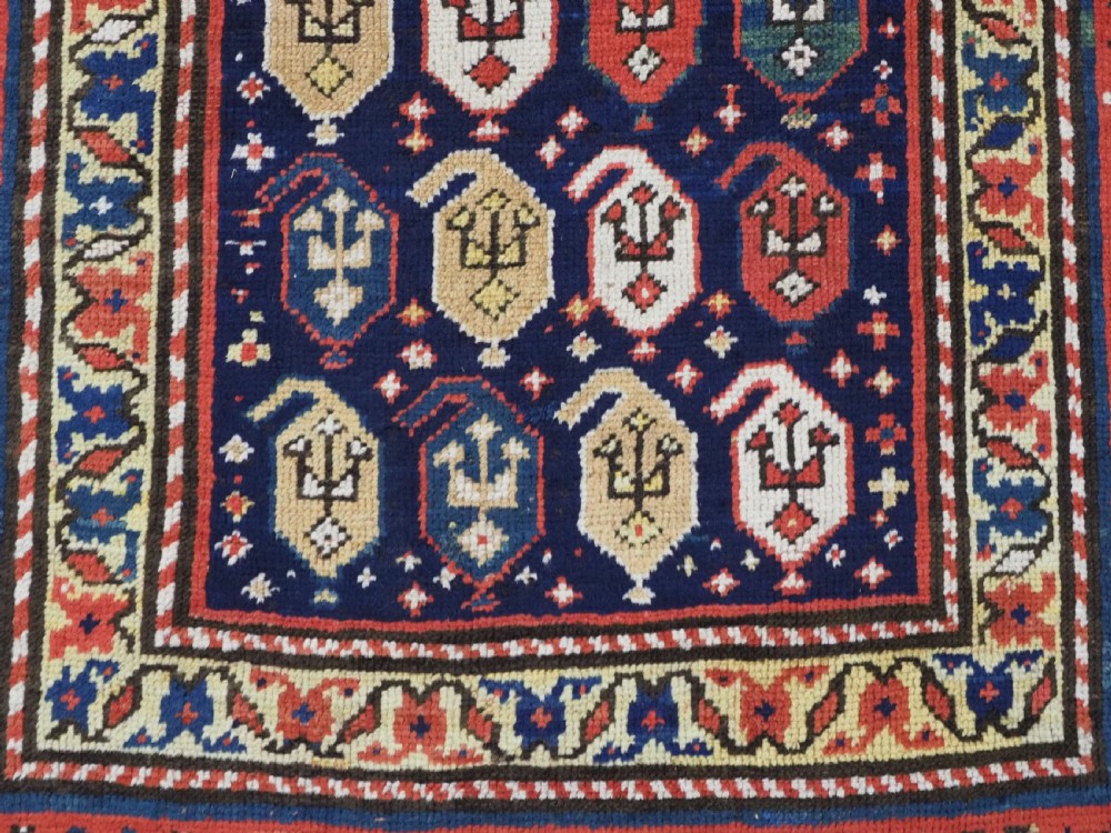 An antique hand-knotted Caucasian runner rug featuring repeated boteh motifs on a dark blue central field framed by red geometric borders. View X