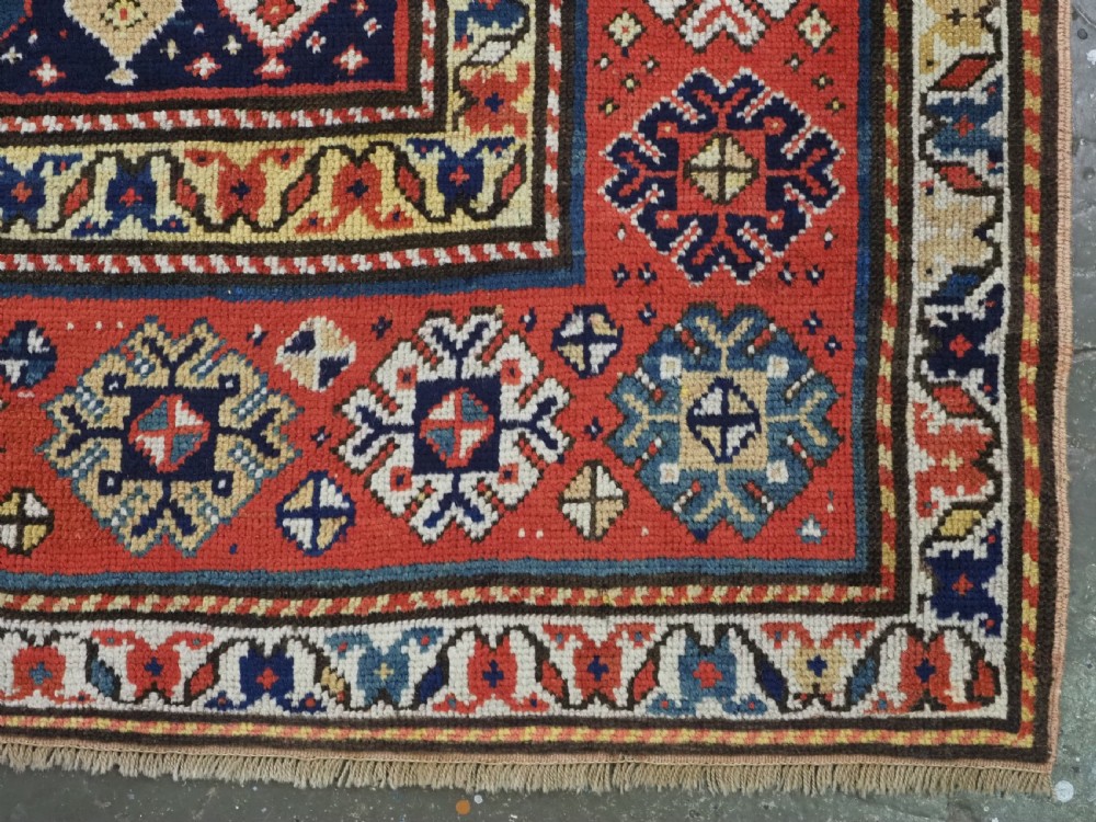 An antique hand-knotted Caucasian runner rug featuring repeated boteh motifs on a dark blue central field framed by red geometric borders. View XI
