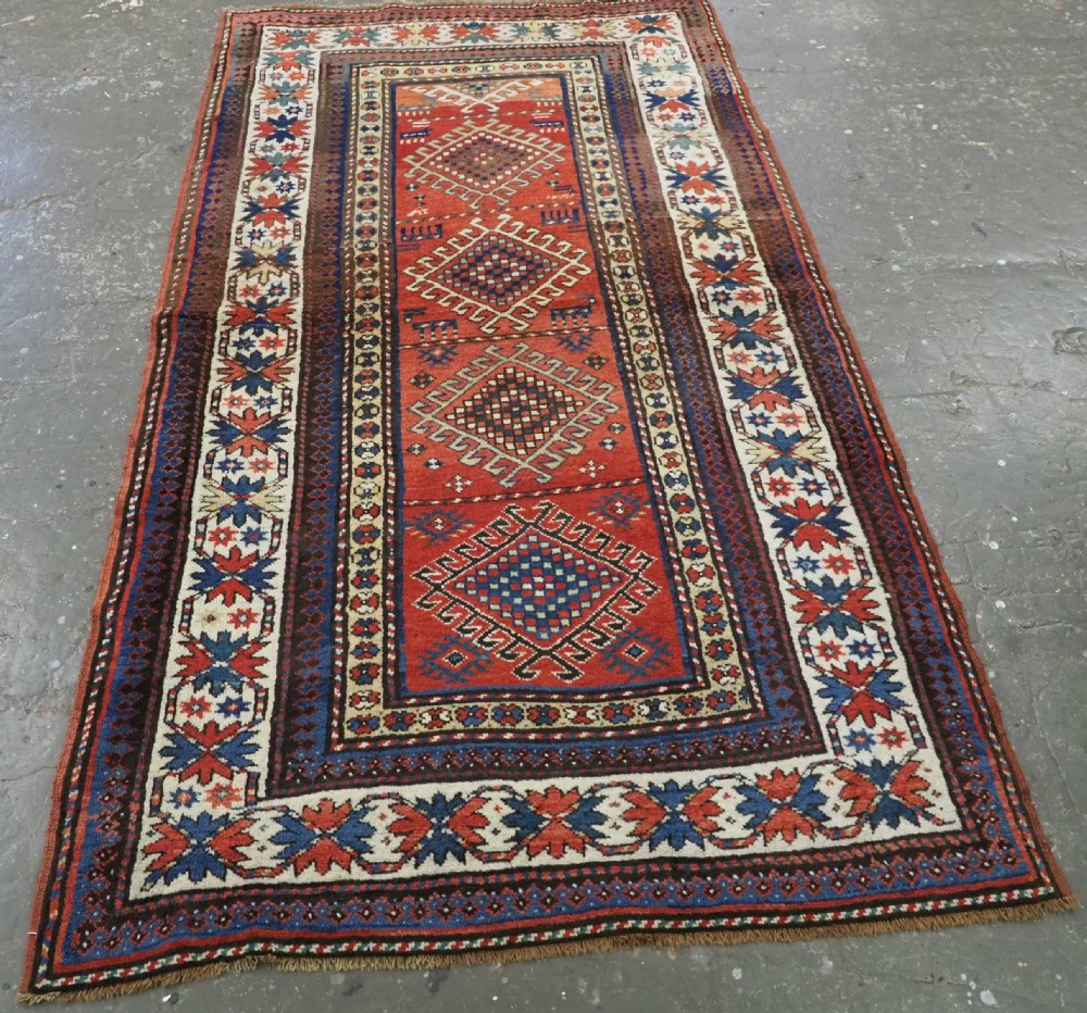 An antique hand-knotted Caucasian Moghan Kazak wool runner featuring four central hooked diamond medallions on a red field enclosed by multi-band geometric borders. View II