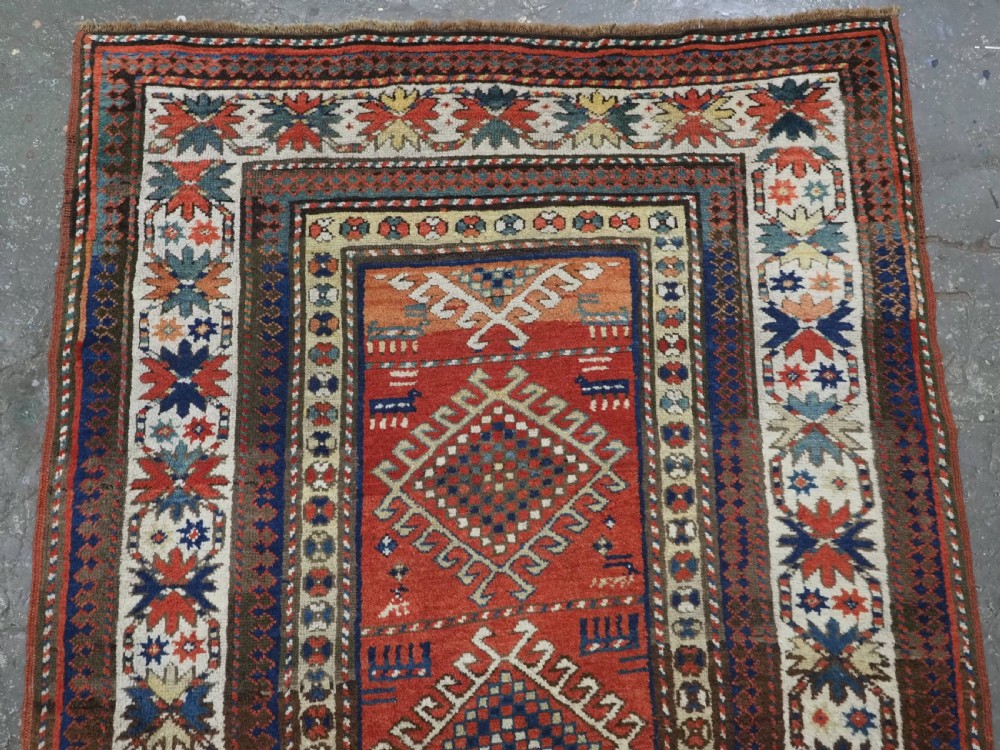 An antique hand-knotted Caucasian Moghan Kazak wool runner featuring four central hooked diamond medallions on a red field enclosed by multi-band geometric borders. View III