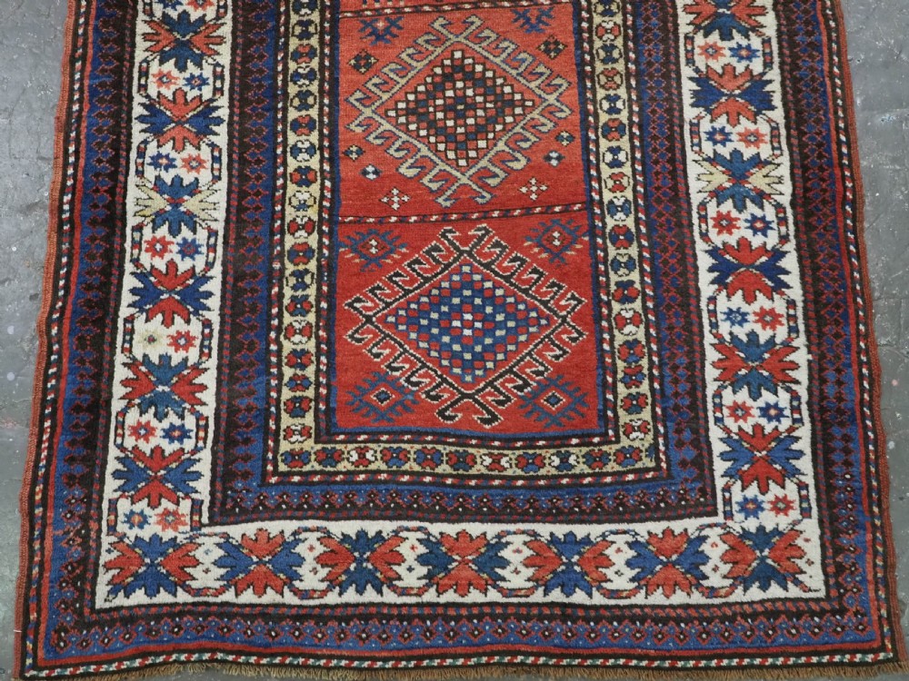An antique hand-knotted Caucasian Moghan Kazak wool runner featuring four central hooked diamond medallions on a red field enclosed by multi-band geometric borders. View IV