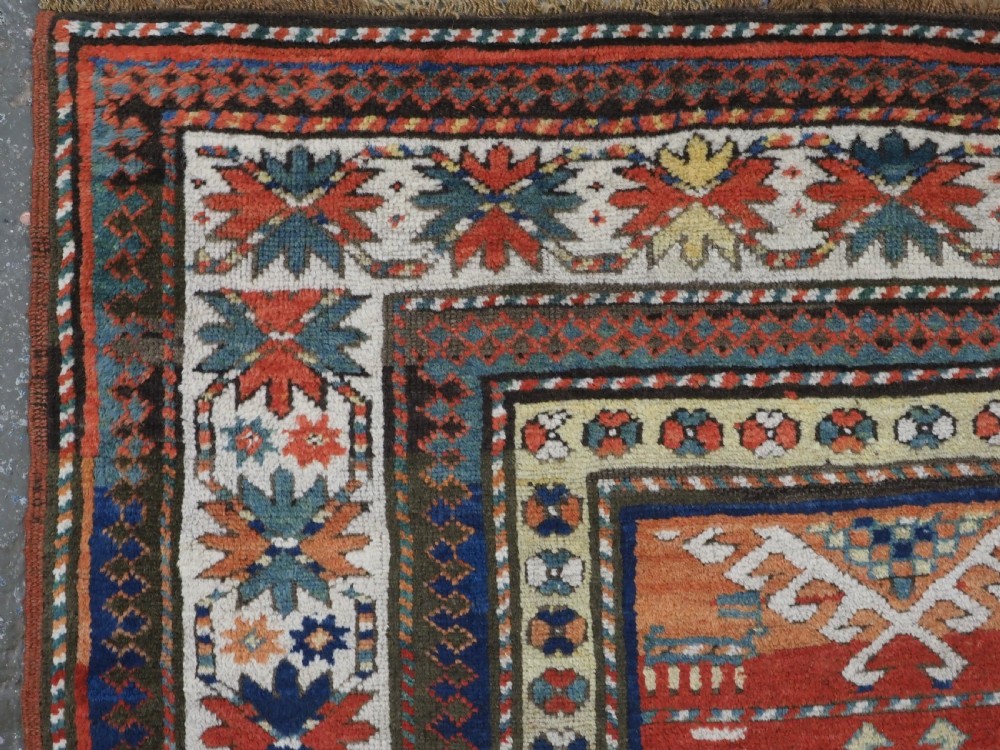 An antique hand-knotted Caucasian Moghan Kazak wool runner featuring four central hooked diamond medallions on a red field enclosed by multi-band geometric borders. View VI