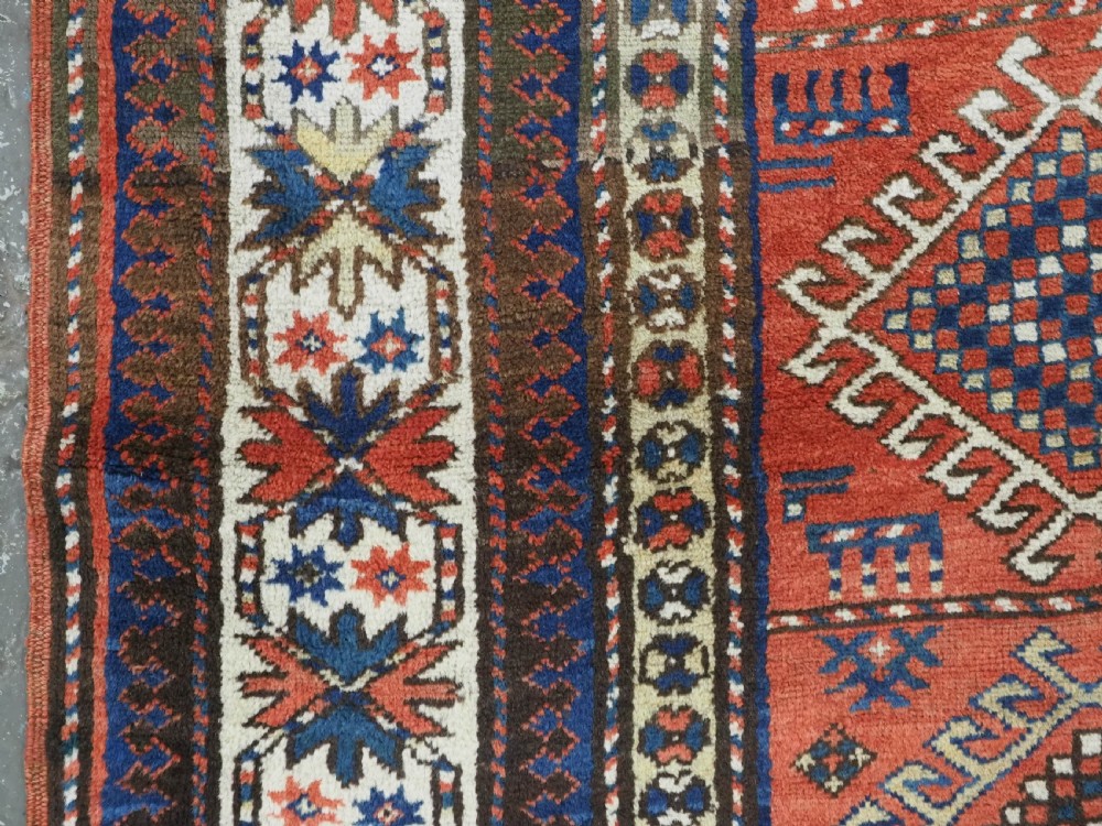 An antique hand-knotted Caucasian Moghan Kazak wool runner featuring four central hooked diamond medallions on a red field enclosed by multi-band geometric borders. View VII
