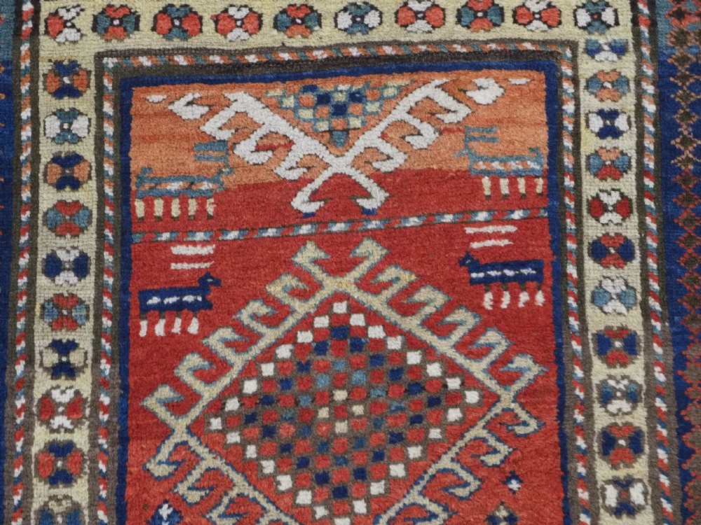 An antique hand-knotted Caucasian Moghan Kazak wool runner featuring four central hooked diamond medallions on a red field enclosed by multi-band geometric borders. View VIII