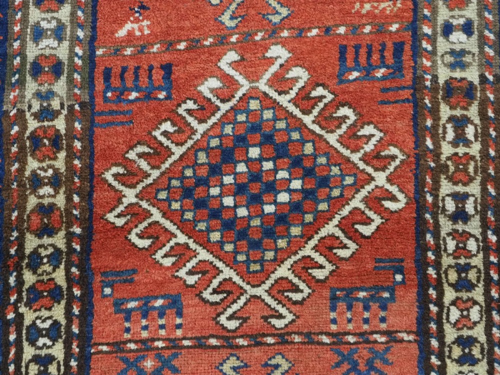 An antique hand-knotted Caucasian Moghan Kazak wool runner featuring four central hooked diamond medallions on a red field enclosed by multi-band geometric borders. View IX
