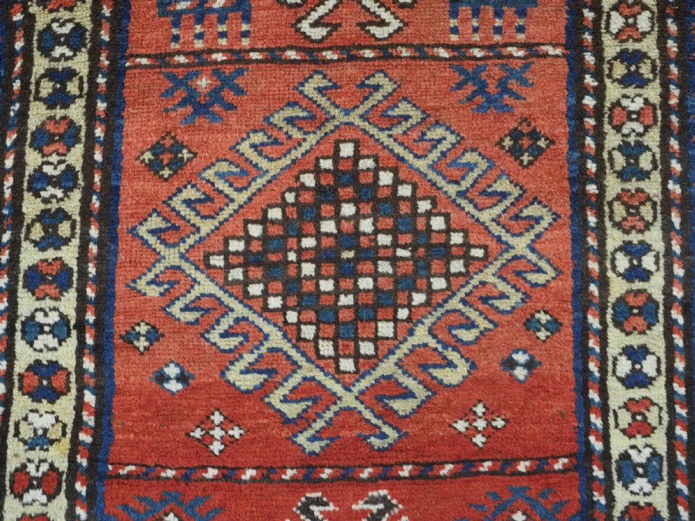 An antique hand-knotted Caucasian Moghan Kazak wool runner featuring four central hooked diamond medallions on a red field enclosed by multi-band geometric borders. View X