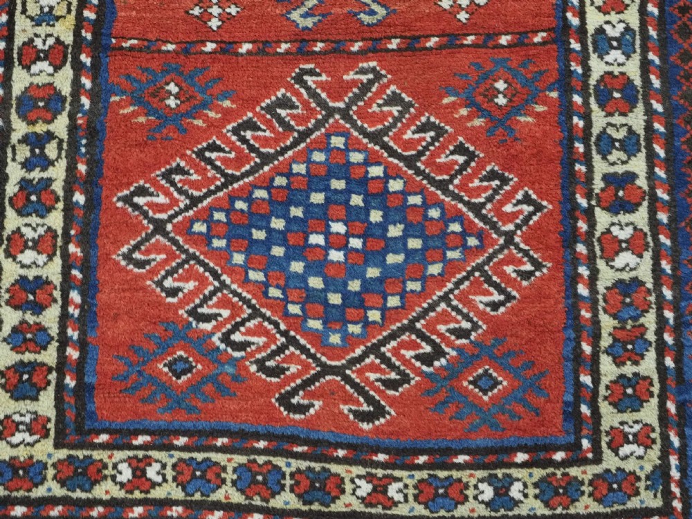 An antique hand-knotted Caucasian Moghan Kazak wool runner featuring four central hooked diamond medallions on a red field enclosed by multi-band geometric borders. View XI