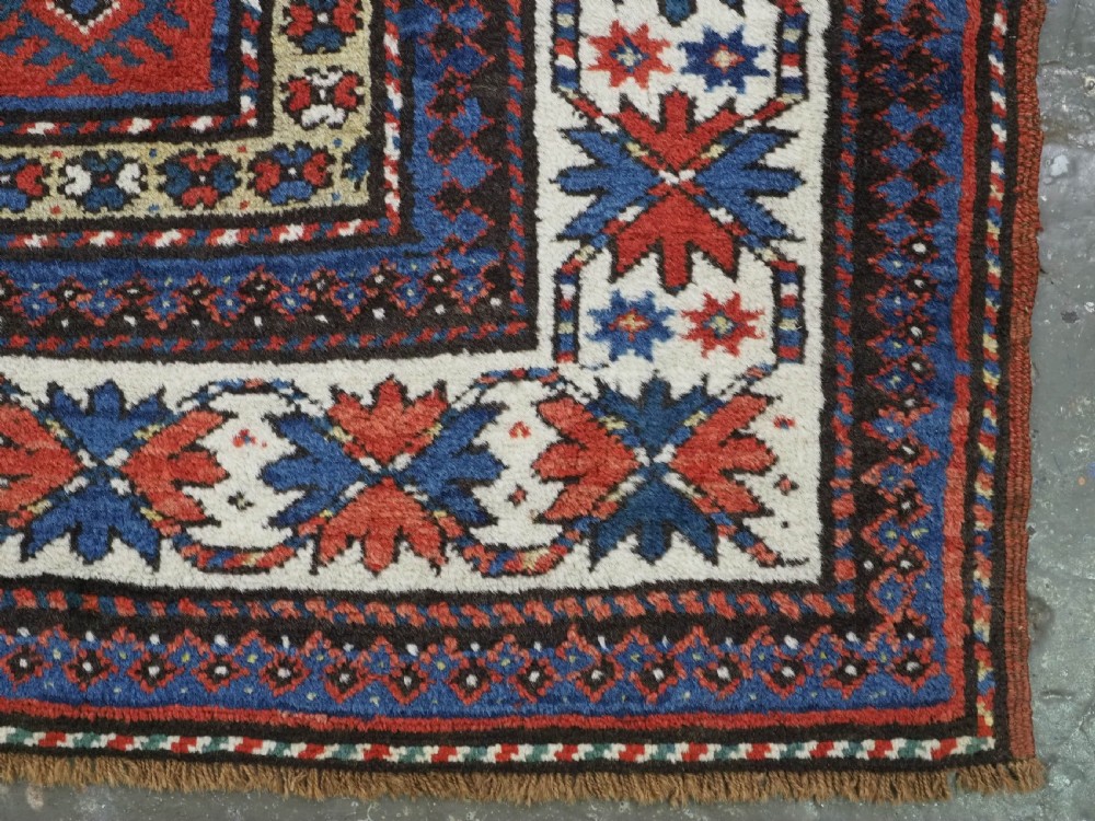 An antique hand-knotted Caucasian Moghan Kazak wool runner featuring four central hooked diamond medallions on a red field enclosed by multi-band geometric borders. View XII