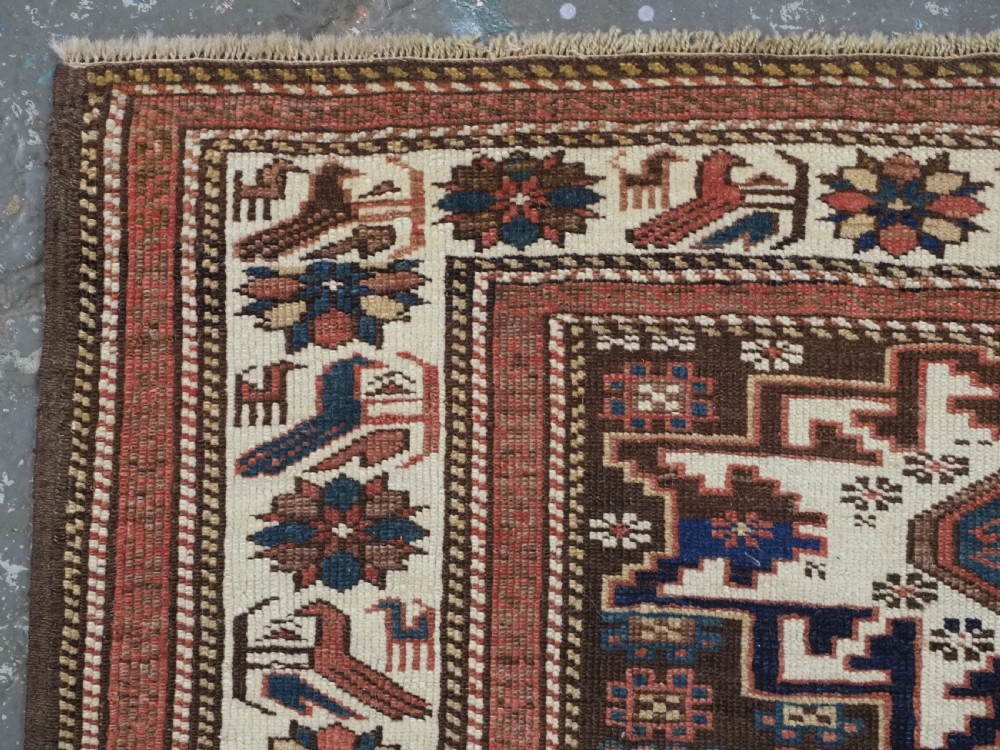 A hand-knotted antique Caucasian wool rug featuring geometric Lesghi star medallions on a dark central field enclosed by an ivory border decorated with stylised bird motifs. View VI