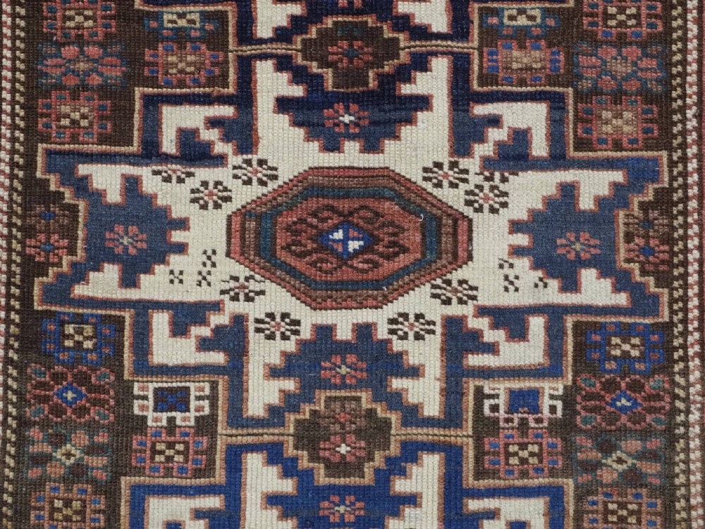 A hand-knotted antique Caucasian wool rug featuring geometric Lesghi star medallions on a dark central field enclosed by an ivory border decorated with stylised bird motifs. View VIII