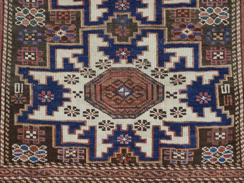 A hand-knotted antique Caucasian wool rug featuring geometric Lesghi star medallions on a dark central field enclosed by an ivory border decorated with stylised bird motifs. View IX