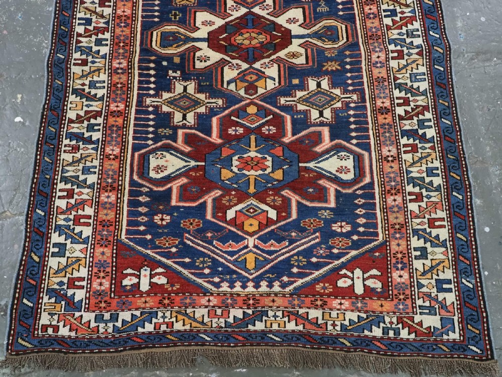 A hand-knotted antique Caucasian rug featuring three lobed medallions on a navy blue field surrounded by intricate geometric borders. View IV
