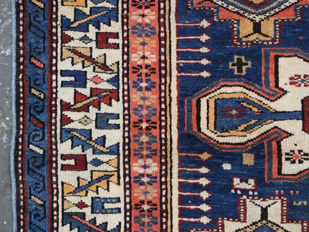 A hand-knotted antique Caucasian rug featuring three lobed medallions on a navy blue field surrounded by intricate geometric borders. View VII