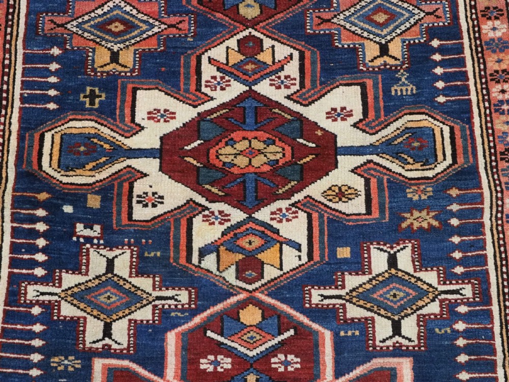 A hand-knotted antique Caucasian rug featuring three lobed medallions on a navy blue field surrounded by intricate geometric borders. View X