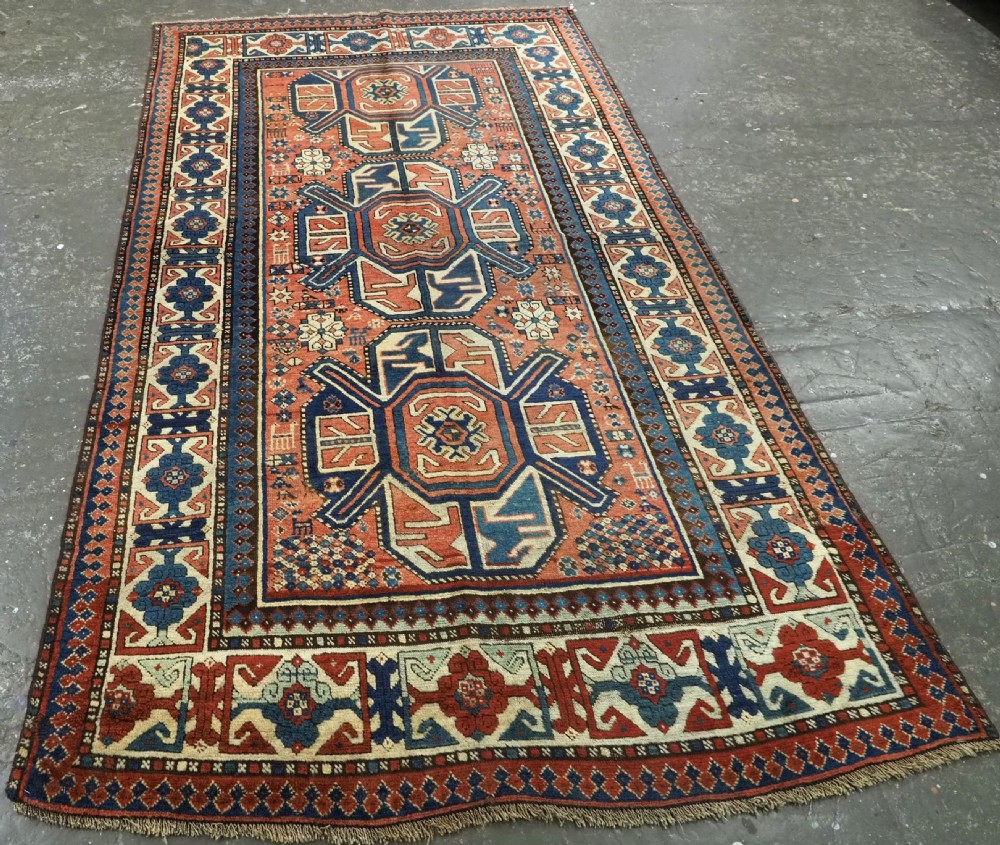An antique hand-knotted Caucasian wool rug featuring three primary geometric medallions on a terracotta field with navy and cream patterned borders. View II