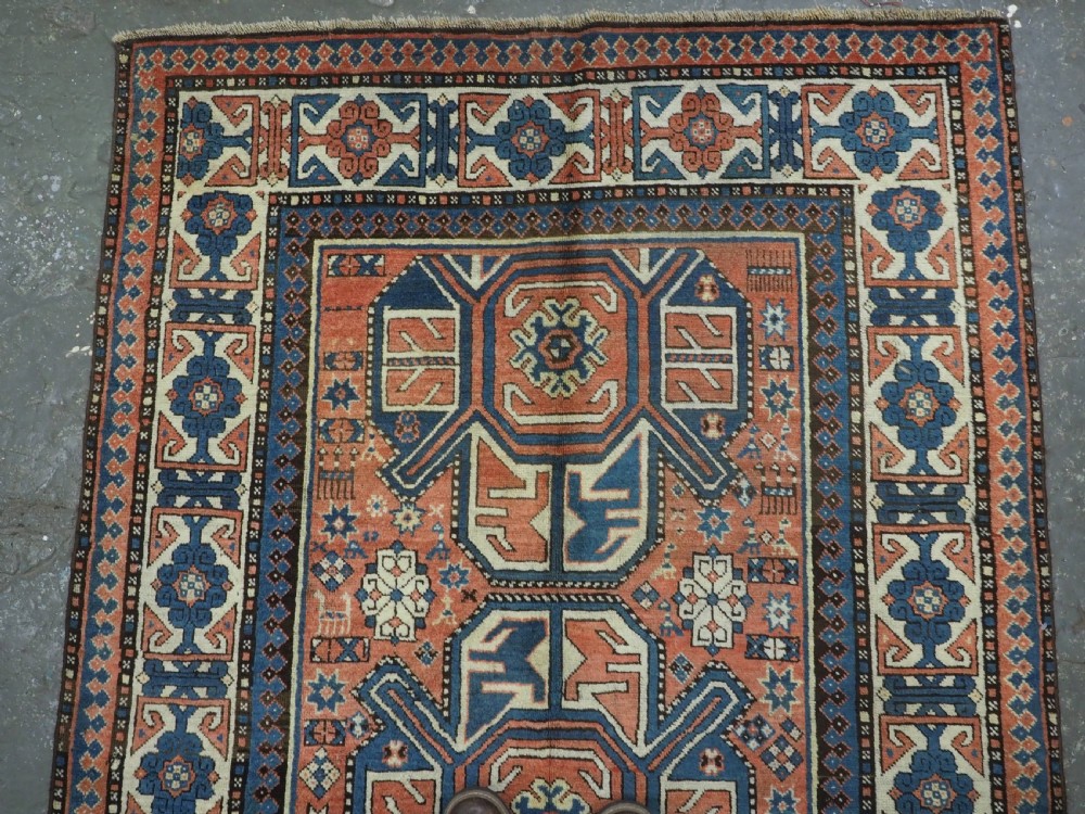 An antique hand-knotted Caucasian wool rug featuring three primary geometric medallions on a terracotta field with navy and cream patterned borders. View III