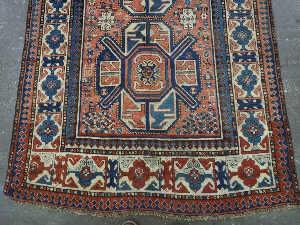 An antique hand-knotted Caucasian wool rug featuring three primary geometric medallions on a terracotta field with navy and cream patterned borders. View V