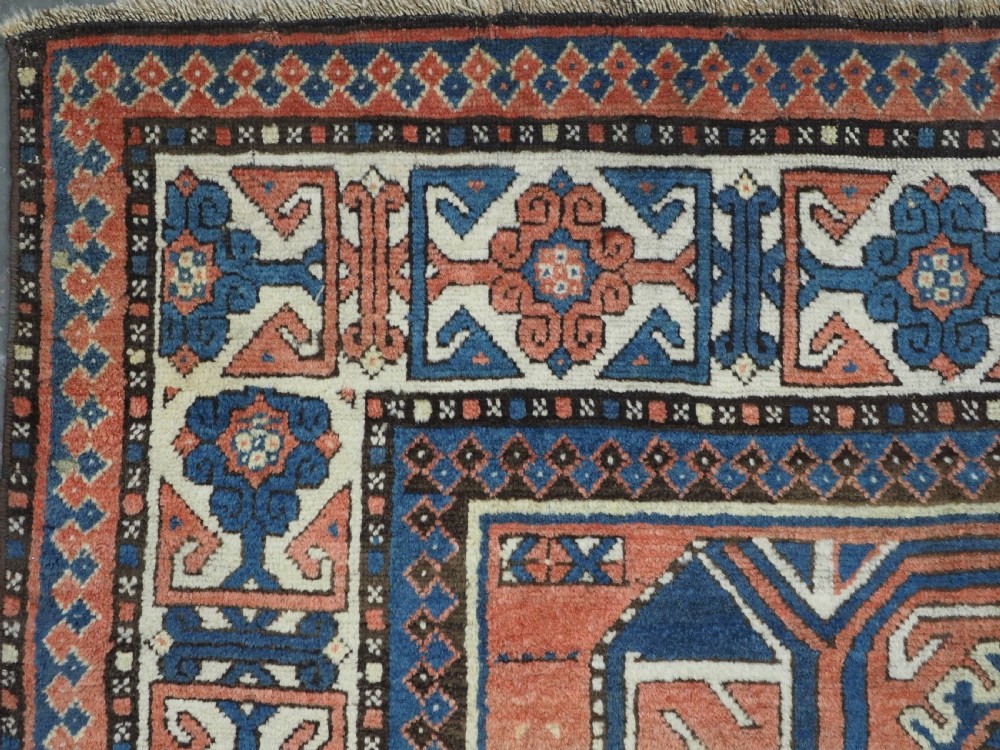 An antique hand-knotted Caucasian wool rug featuring three primary geometric medallions on a terracotta field with navy and cream patterned borders. View VI