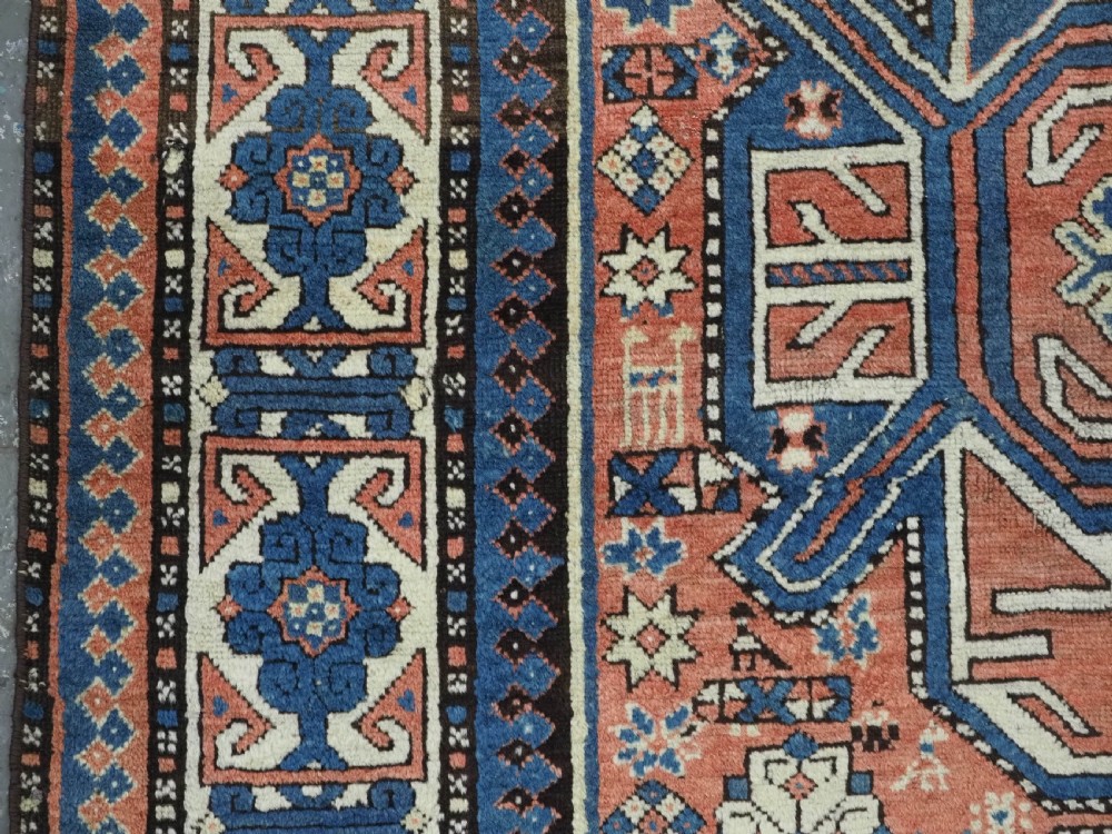 An antique hand-knotted Caucasian wool rug featuring three primary geometric medallions on a terracotta field with navy and cream patterned borders. View VII