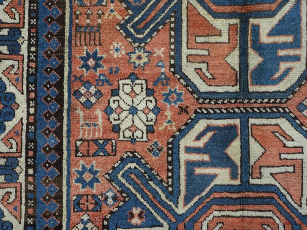 An antique hand-knotted Caucasian wool rug featuring three primary geometric medallions on a terracotta field with navy and cream patterned borders. View VIII