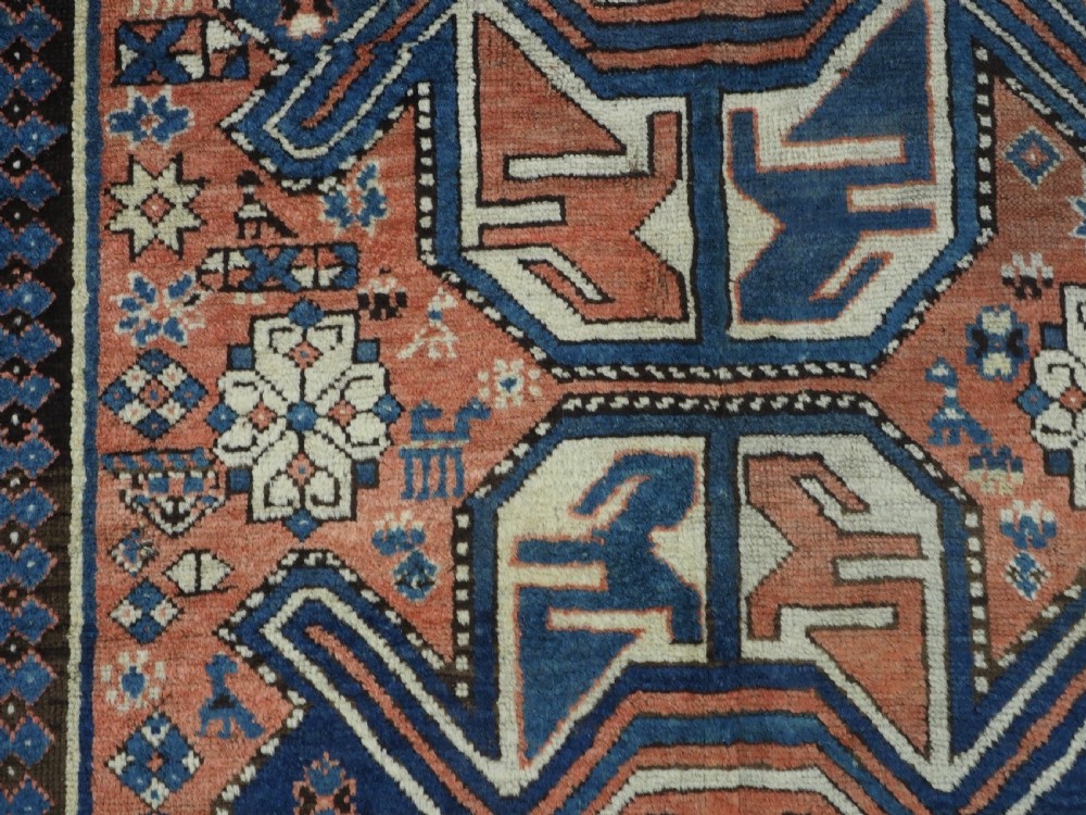 An antique hand-knotted Caucasian wool rug featuring three primary geometric medallions on a terracotta field with navy and cream patterned borders. View IX