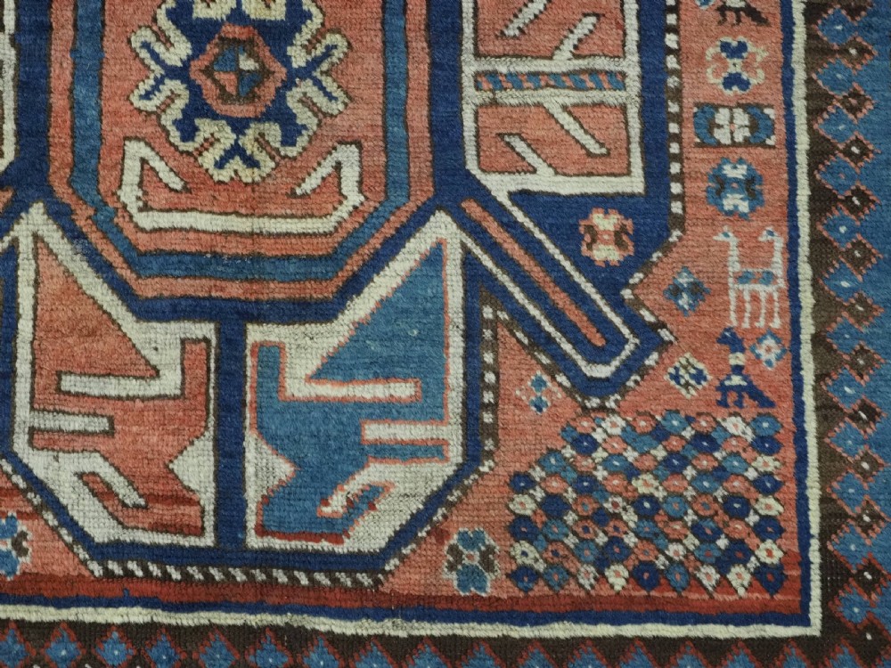 An antique hand-knotted Caucasian wool rug featuring three primary geometric medallions on a terracotta field with navy and cream patterned borders. View X