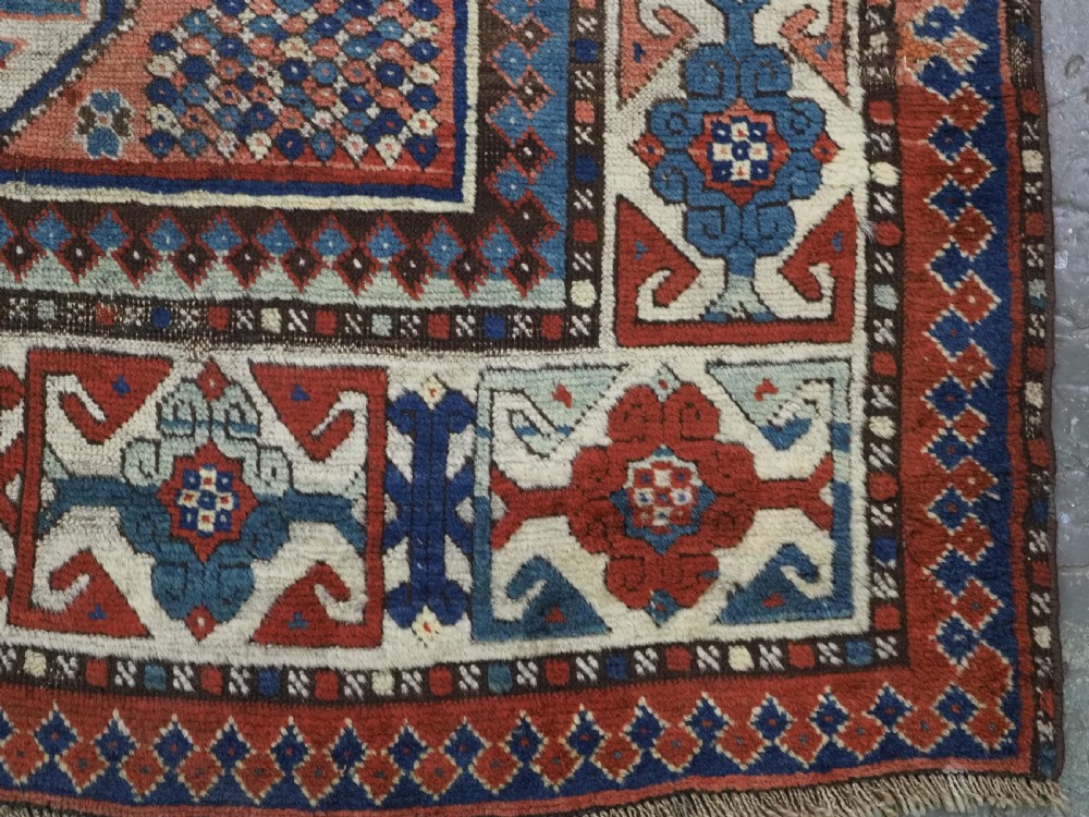An antique hand-knotted Caucasian wool rug featuring three primary geometric medallions on a terracotta field with navy and cream patterned borders. View XI