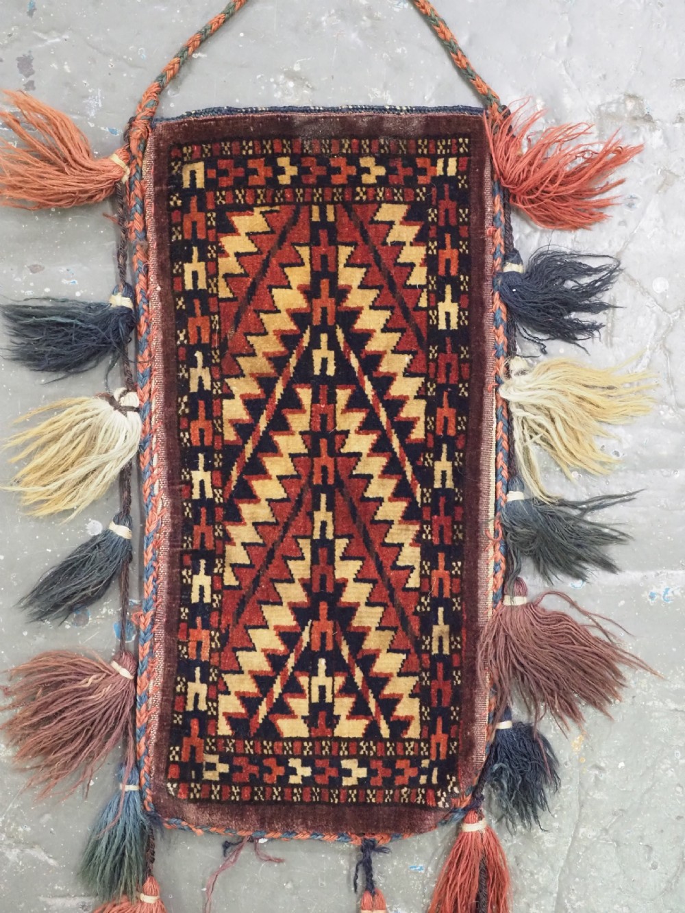 A narrow hand-knotted wool Turkmen spindle bag featuring chevron geometric patterns in terracotta, yellow, and dark brown with long side and bottom tassels. View II