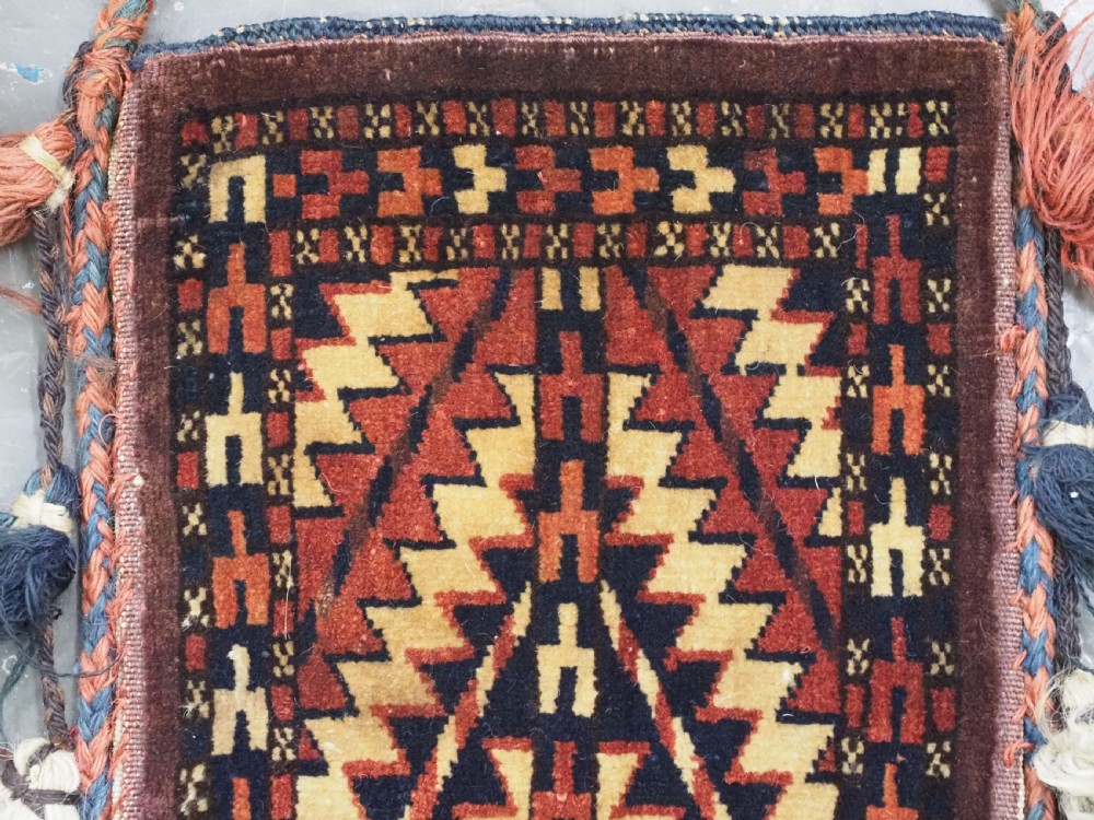 A narrow hand-knotted wool Turkmen spindle bag featuring chevron geometric patterns in terracotta, yellow, and dark brown with long side and bottom tassels. View III