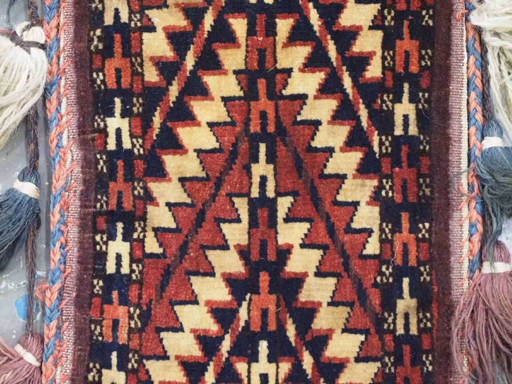 A narrow hand-knotted wool Turkmen spindle bag featuring chevron geometric patterns in terracotta, yellow, and dark brown with long side and bottom tassels. View IV