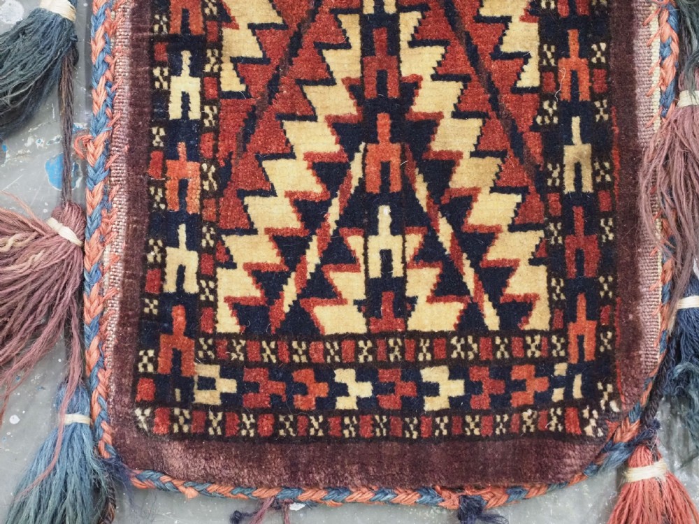 A narrow hand-knotted wool Turkmen spindle bag featuring chevron geometric patterns in terracotta, yellow, and dark brown with long side and bottom tassels. View V