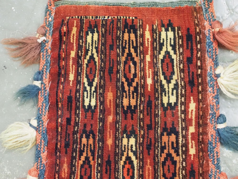 A narrow hand-knotted wool Yomut Turkmen spindle bag with rust red geometric vertical patterns, multi-coloured tassels along the edges, and a braided hanging loop. View II