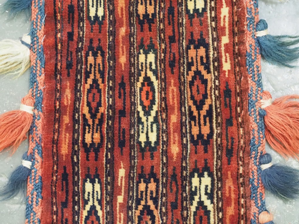 A narrow hand-knotted wool Yomut Turkmen spindle bag with rust red geometric vertical patterns, multi-coloured tassels along the edges, and a braided hanging loop. View III