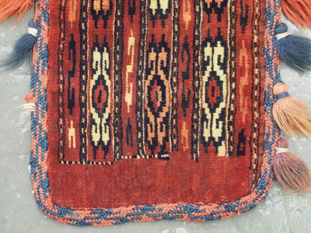 A narrow hand-knotted wool Yomut Turkmen spindle bag with rust red geometric vertical patterns, multi-coloured tassels along the edges, and a braided hanging loop. View IV