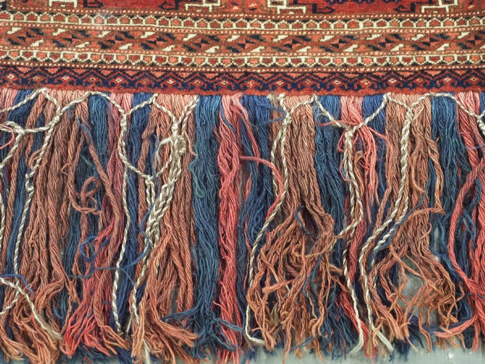 An antique rectangular handwoven Tekke Turkmen wool torba featuring four geometric octagonal guls on a deep red field with long multi-coloured fringe along the bottom edge. View VI