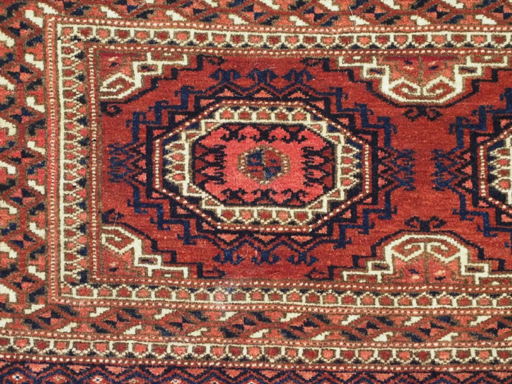 An antique rectangular handwoven Tekke Turkmen wool torba featuring four geometric octagonal guls on a deep red field with long multi-coloured fringe along the bottom edge. View VIII