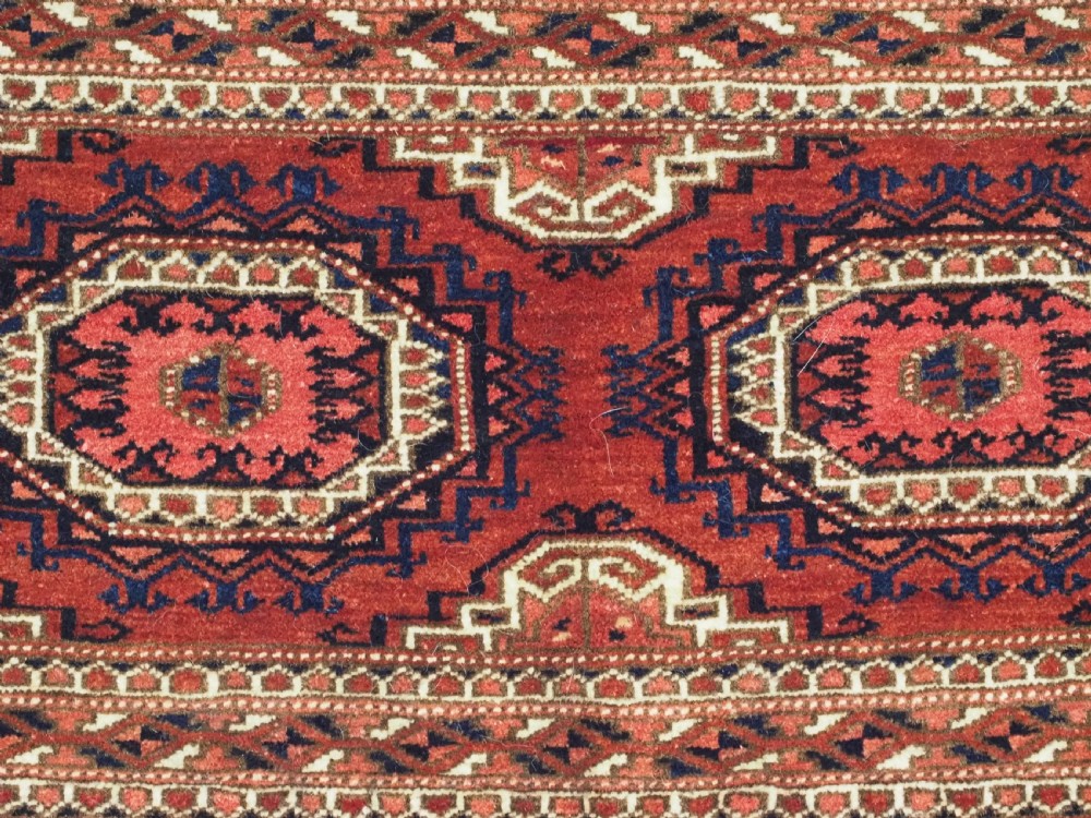 An antique rectangular handwoven Tekke Turkmen wool torba featuring four geometric octagonal guls on a deep red field with long multi-coloured fringe along the bottom edge. View IX