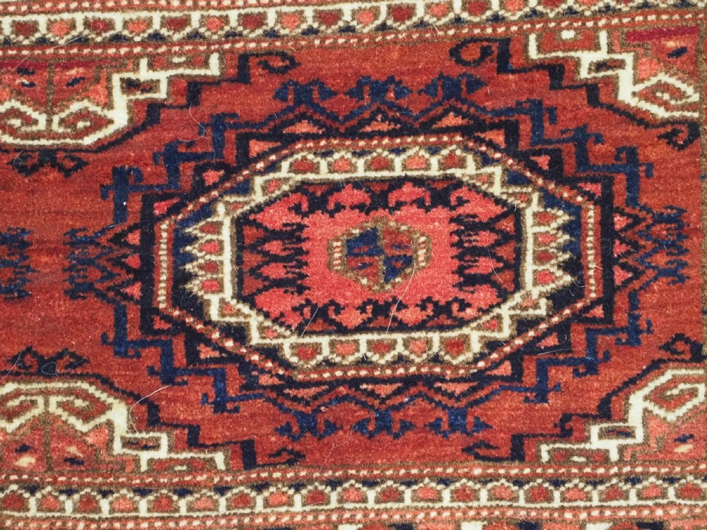 An antique rectangular handwoven Tekke Turkmen wool torba featuring four geometric octagonal guls on a deep red field with long multi-coloured fringe along the bottom edge. View X