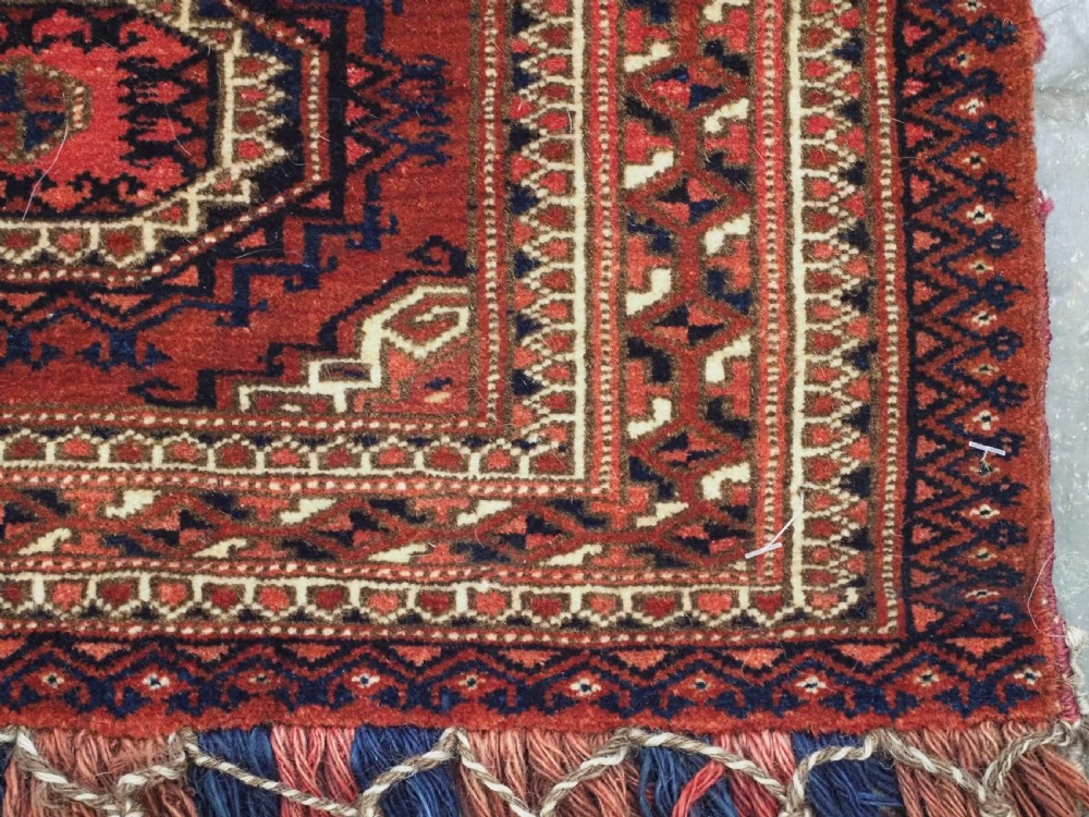 An antique rectangular handwoven Tekke Turkmen wool torba featuring four geometric octagonal guls on a deep red field with long multi-coloured fringe along the bottom edge. View XI