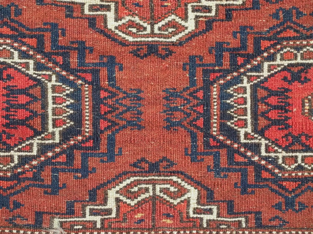 An antique rectangular handwoven Tekke Turkmen wool torba featuring four geometric octagonal guls on a deep red field with long multi-coloured fringe along the bottom edge. View XII