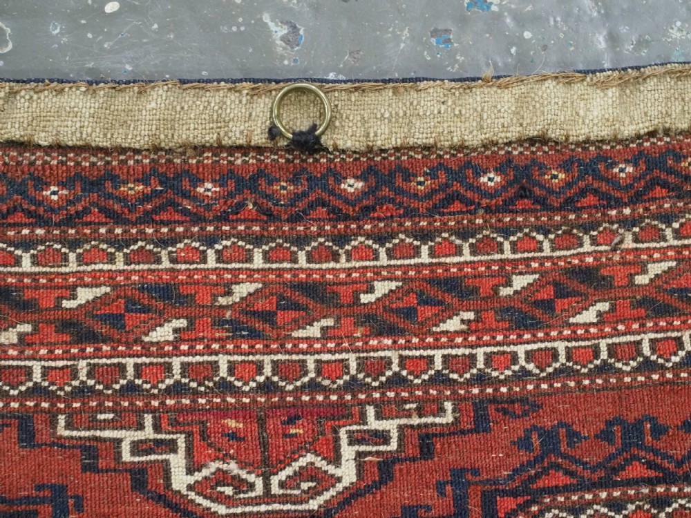 An antique rectangular handwoven Tekke Turkmen wool torba featuring four geometric octagonal guls on a deep red field with long multi-coloured fringe along the bottom edge. View XIII