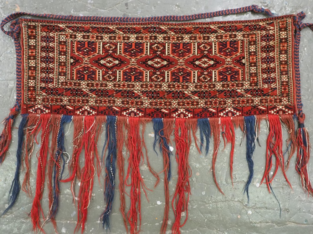 Horizontal handwoven Turkmen wool torba bag featuring deep red and indigo geometric kedjebe motifs with long woollen fringe along the bottom edge.