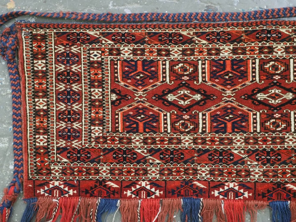 Horizontal handwoven Turkmen wool torba bag featuring deep red and indigo geometric kedjebe motifs with long woollen fringe along the bottom edge. View III