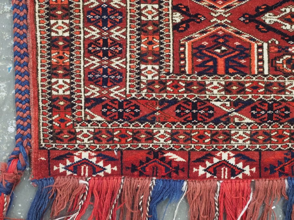 Horizontal handwoven Turkmen wool torba bag featuring deep red and indigo geometric kedjebe motifs with long woollen fringe along the bottom edge. View V