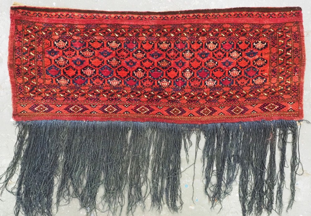 A horizontal rectangular hand-knotted Turkmen torba with repeating red and blue Shemle guls and long wool fringe along the lower border.