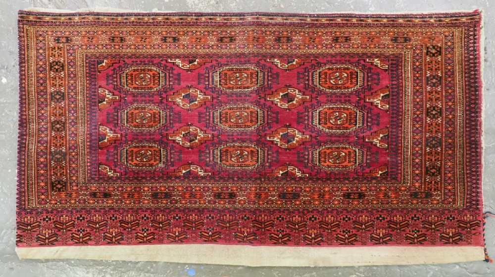 A rectangular hand-knotted crimson red Turkmen chuval featuring nine central octagonal Salor guls framed by ornate geometric borders and a decorative lower elem panel.